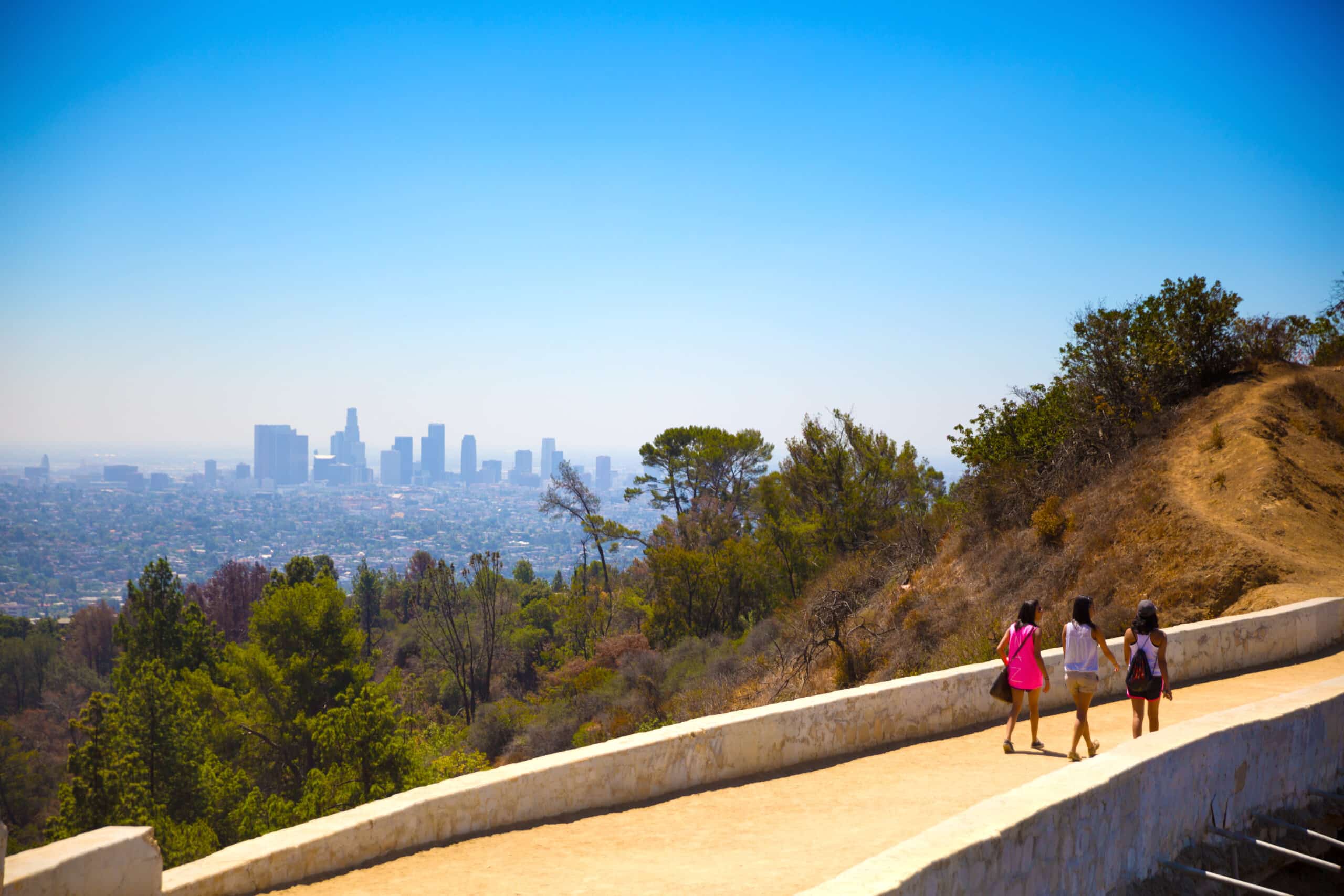 Tourists walking along mountain path with Los Angeles city skyline in the distance